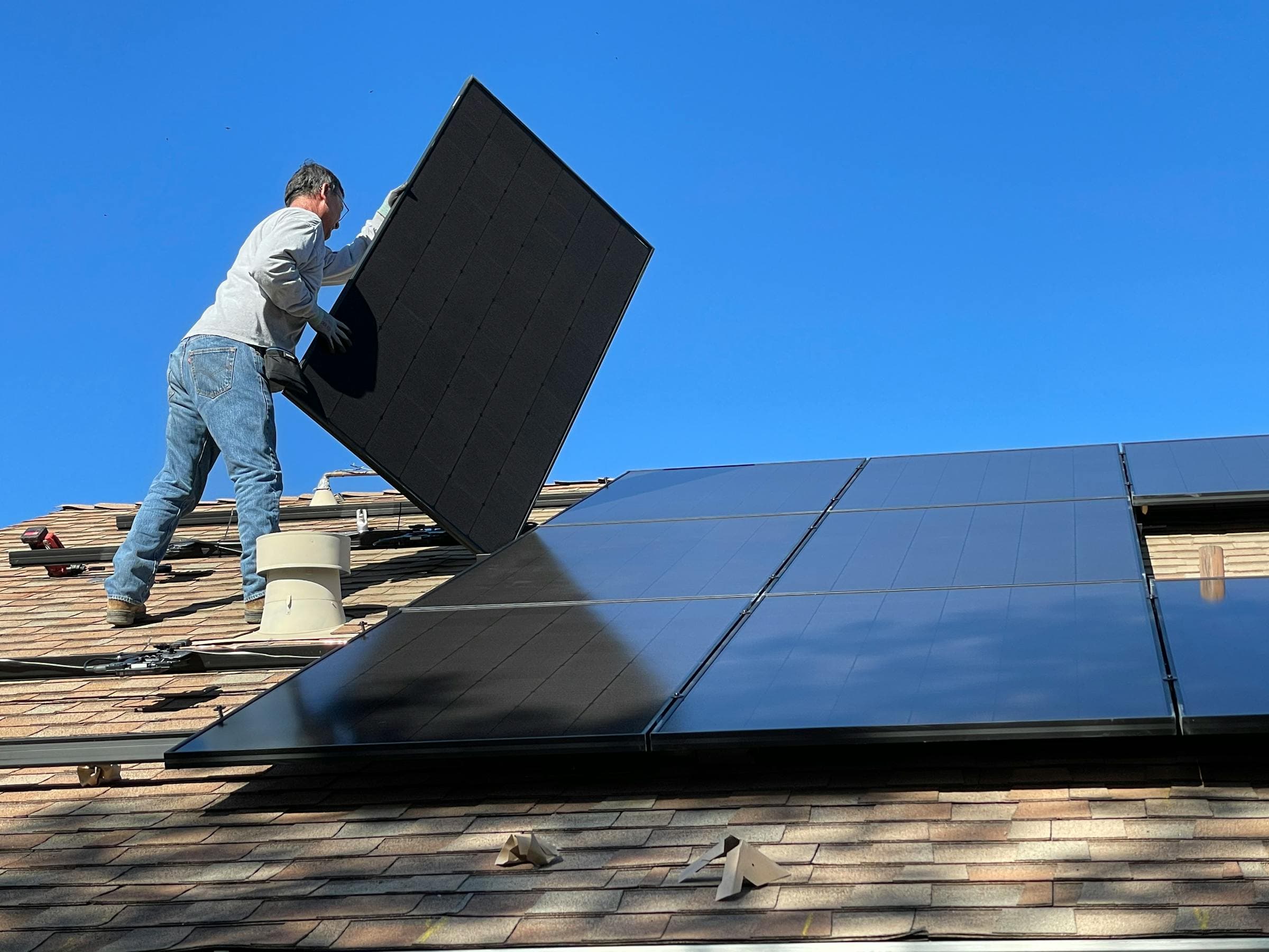 A solar installer mounting a panel on a rooftop under a blue sky